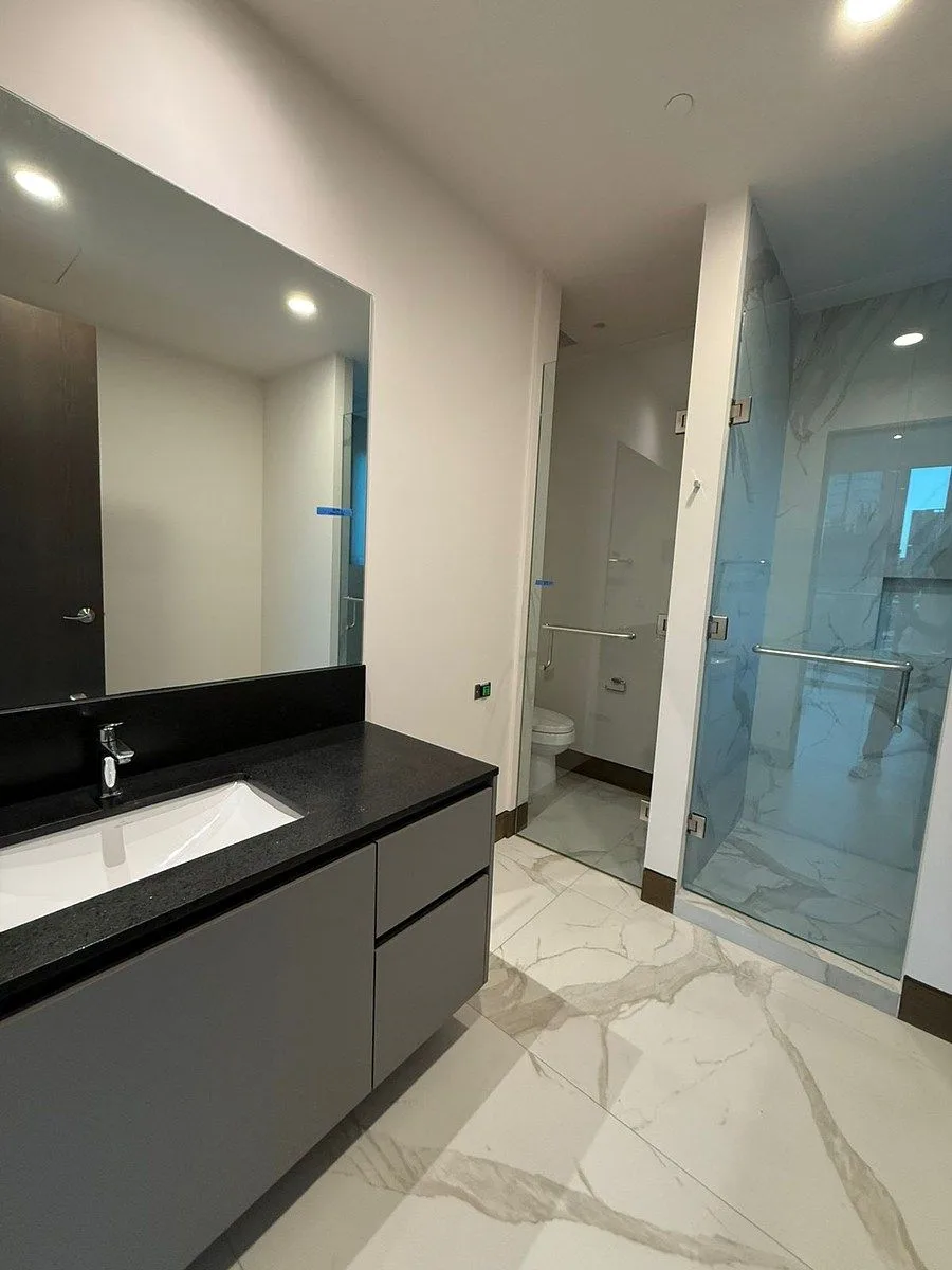 baño completo con canceles de cristal y cubiertas oscuras